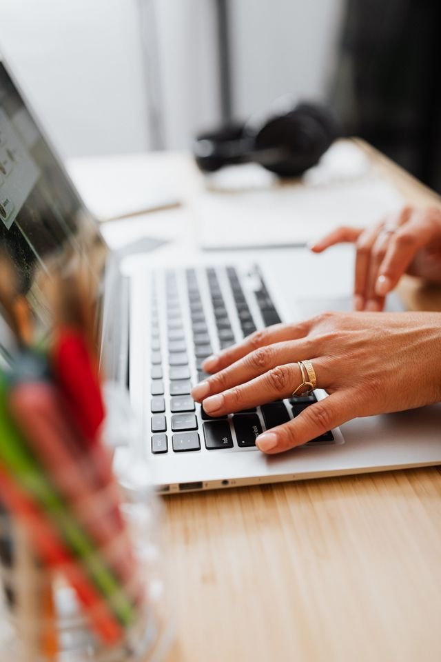 Hände tippen auf einer Laptop-Tastatur, um eine Transkription zu erstellen, im Hintergrund liegen Kopfhörer.